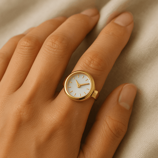 Goldene Fingeruhr mit kleinem Zifferblatt, getragen am Zeigefinger auf hellem Stoffhintergrund